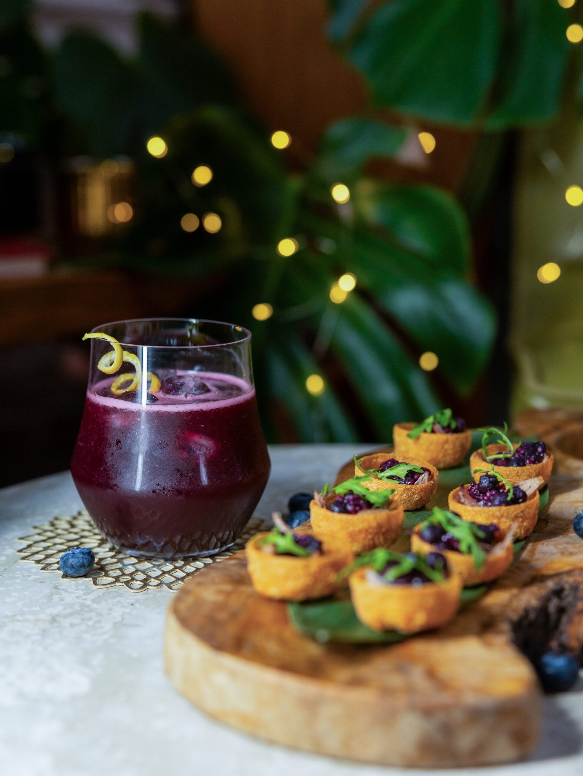 A festive blueberry spirit free cocktail with duck canapés and holiday lights.